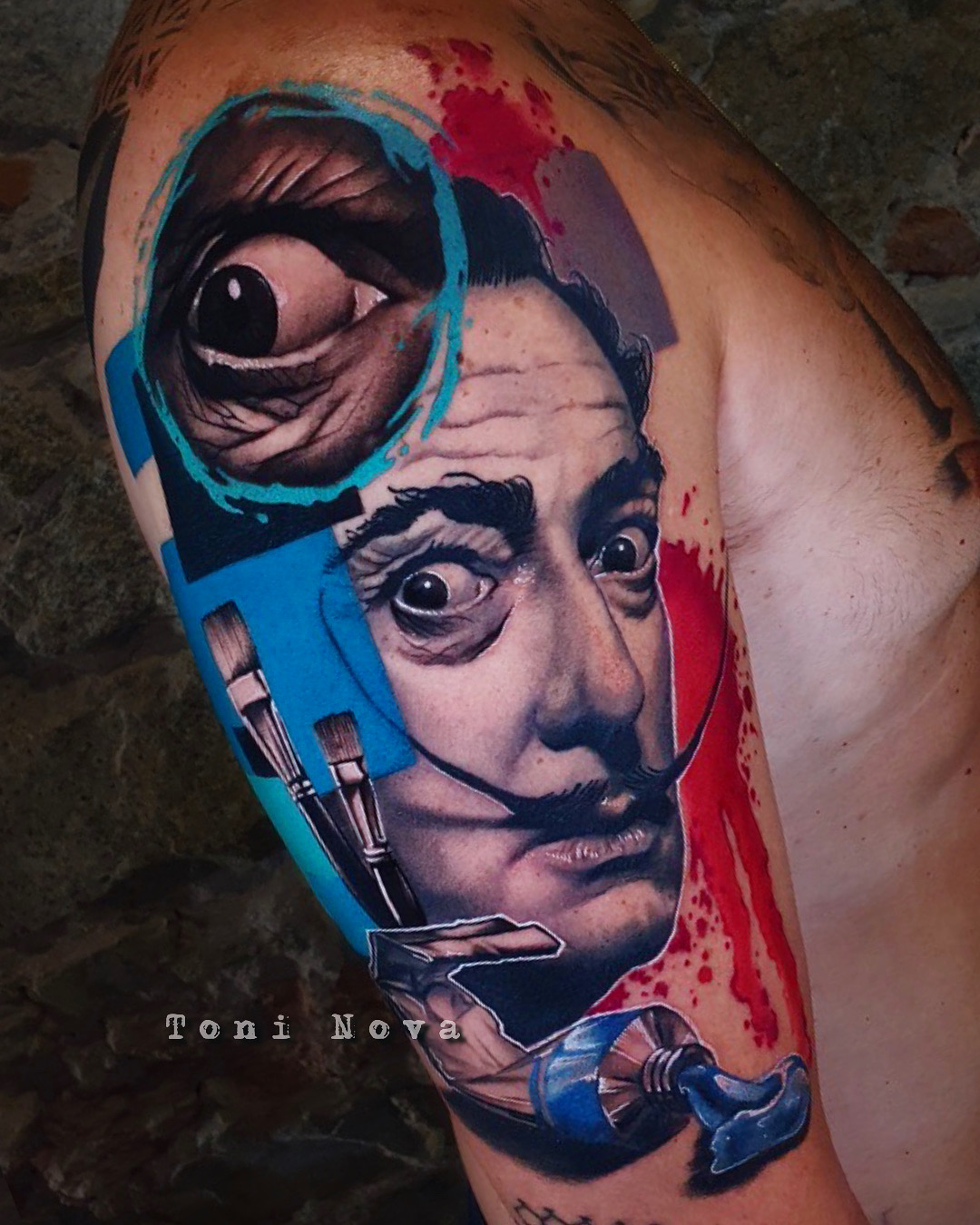 Tatuaje de Dalí por Toni Nova: retrato realista con pinceles, azul y rojo